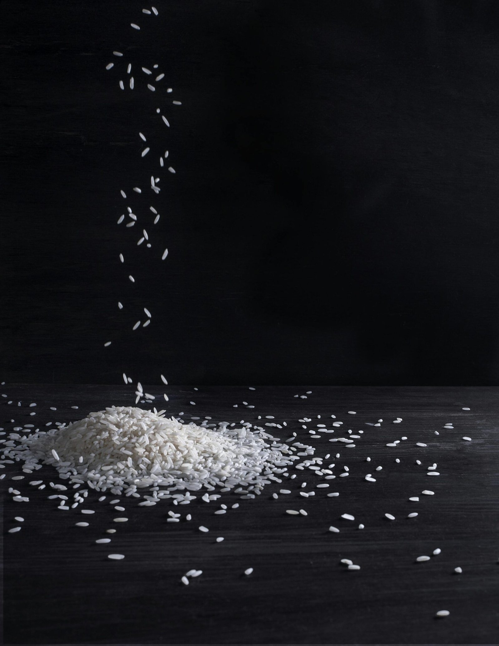 A minimalist still life capturing rice falling on a dark wooden surface in a studio setting.